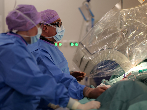 Zwei Operateure mit OP-Kleidung, Kopfhauben und Mundschutz blicken während einer Operation in Richtung des hell erleuchteten Operationsfelds im Albertinen Herz- und Gefäßzentrum am Standort Amalie Sieveking Krankenhaus Zwei Operateure mit OP-Kleidung, Kopfhauben und Mundschutz blicken während einer Operation in Richtung des hell erleuchteten Operationsfelds im Albertinen Herz- und Gefäßzentrum am Standort Amalie Sieveking Krankenhaus