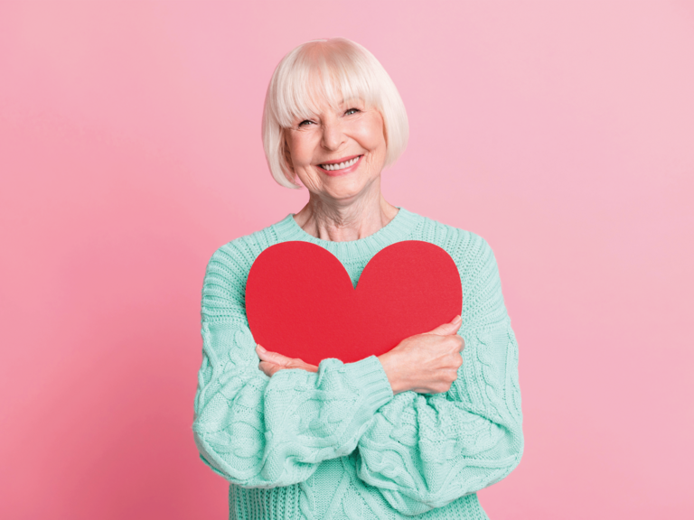 Eine Frau lächelt mit einem großen Papierherz in den Armen in die Kamera Eine Frau lächelt mit einem großen Papierherz in den Armen in die Kamera